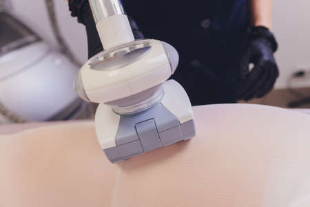 Parts of female body in special white suit having anti cellulite massage with spa apparatus.
