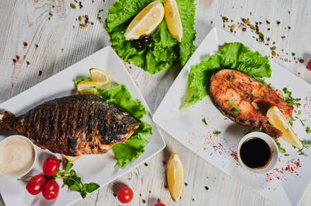 Dorado fish garnished with vegetables, herbs and lemon on a dish.の写真素材