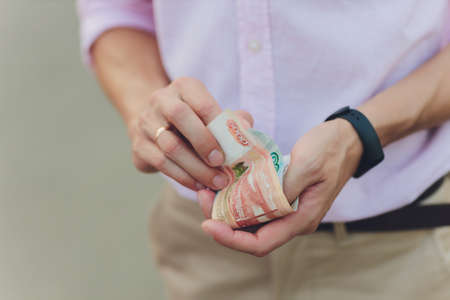 A close up photo of a Caucasian male hand holding a 100 Russian ruble note.