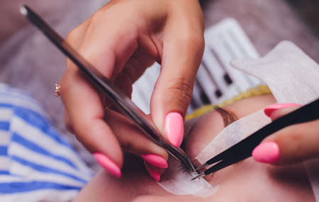 Bunch of artificial eyelashes in tweezers. Extensions of artificial eyelash, process close up. Woman in a beauty salon. Beauty and self-care.の写真素材