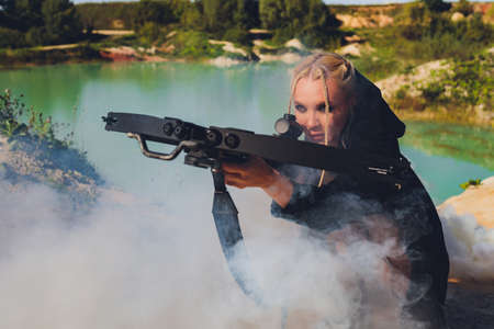 Beautiful woman soldier holding a rifle standing on a rock on the mountain.blue sky hot sun.の写真素材