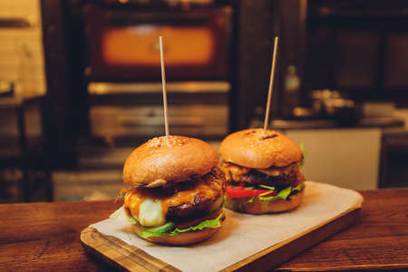 Close-up of delicious fresh home made burger with lettuce, cheese, onion and tomato on a rustic wooden plank on a dark background. Also fries and Cola with ice.の写真素材