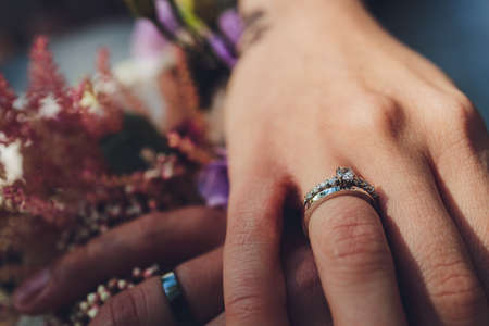 Closeup view of newlyweds hands holding colorful wedding bouquet. Bride and groom wearing wedding rings. Outdoor background. Wedding day concept.の写真素材