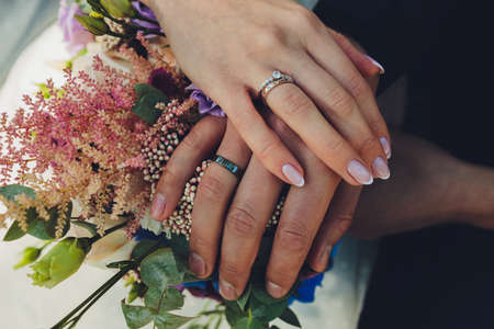 Closeup view of newlyweds hands holding colorful wedding bouquet. Bride and groom wearing wedding...
