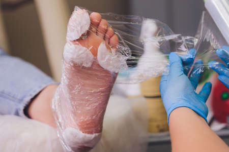 Hands in gloves cares foot nails. Pedicure beauty salon. Foot moisturizing cream.