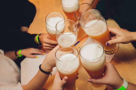 Close up shot of group of people clinking glasses with beer in front of bokeh background. older...