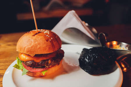 Tasty grilled beef burger with lettuce, ketchup, onion rings, chili and mayonnaise served on pieces of brown paper on a rustic wooden table of counter, with copyspace.の写真素材
