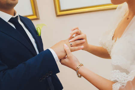 Newlyweds exchange rings, groom puts the ring on the brides hand in marriage registry office.の写真素材
