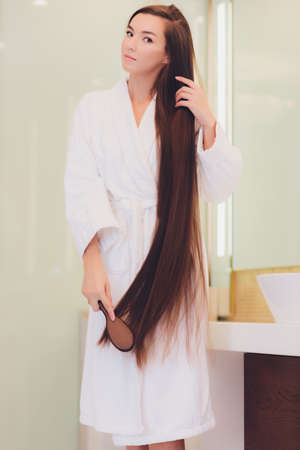 Young pregnant woman brushes long hair in a bathroom.の写真素材