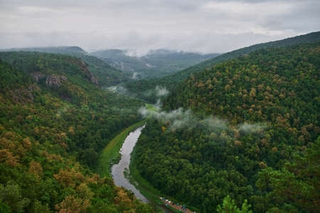 Panoramic aerial view over the top of a summer landscape of a green hills, a large river, and a forest belt at sunset, captured from a helicopter as a birds eye view.の写真素材