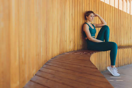Beautiful young fitness instructor gives lessons on video using laptop on a wooden veranda on the street.の写真素材