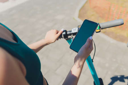 Unrecognizable female using smartphone to pay for rental electric scooter while standing on parking...