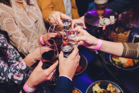 Close up shot of group of people clinking glasses with wine or champagne in front of bokeh...