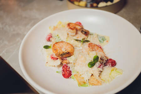 On a square white plate, a serving of Caesar salad with shrimp. Appetizing seafood. Grated Parmesan. Close up, selective focus.の写真素材