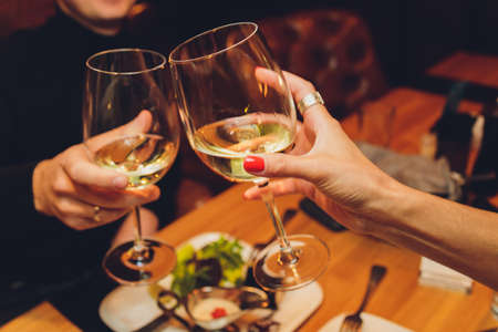 Close up shot of group of people clinking glasses with wine or champagne in front of bokeh...