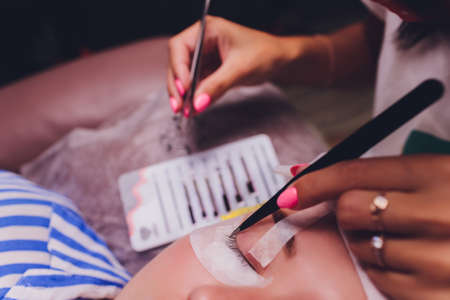 Bunch of artificial eyelashes in tweezers. Extensions of artificial eyelash, process close up. Woman in a beauty salon. Beauty and self-care.の写真素材