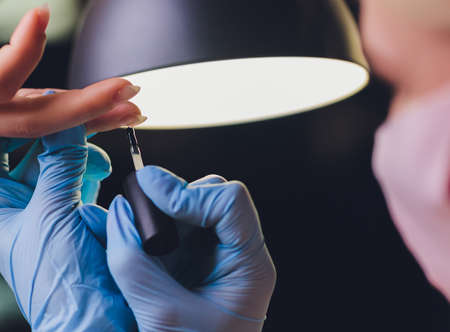 Close-up of beautician applying colorful varnish. Applying nail polish on nails with a brush for...