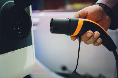 Color image of a mans hand preparing to charge an electric car.