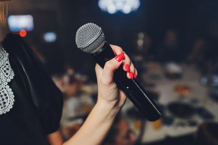 Microphone and unrecognizable female singer close up. Cropped image of female singer in pink dress , singing into a microphone, holding mic with two hands. Copyspace.の写真素材