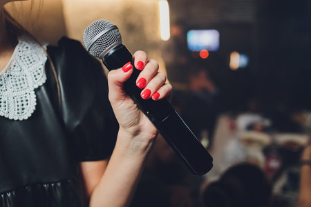 Microphone and unrecognizable female singer close up. Cropped image of female singer in pink dress , singing into a microphone, holding mic with two hands. Copyspace.の写真素材