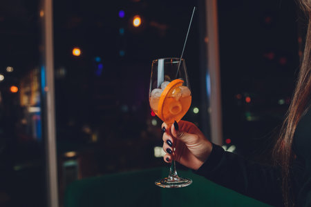 a girl holds in her hand a transparent glass of red cocktail, ice cubes float in the glass.の写真素材