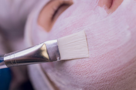 Top view of beautiful young woman getting face skin treatment. Cosmetician is undertaking the procedure applying cream.の写真素材