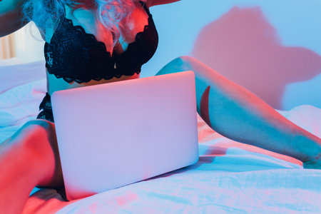 Beautiful, young girl posing in front of a web camera, working as a sexual model. The concept of online flirting, sex on the Internet.の写真素材