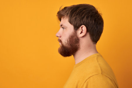 Perfect beard. Close-up of young bearded man standing against yellow isolated background.の写真素材