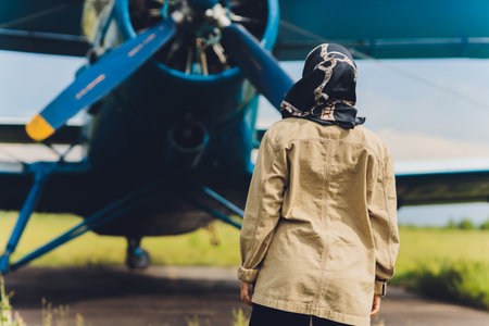 a young Muslim woman in a headscarf stands against the background of an old plane.