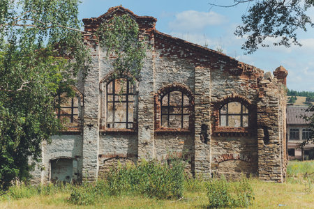 the remains of a derelict abandoned stone house covered in moss and overgrown with trees in a...