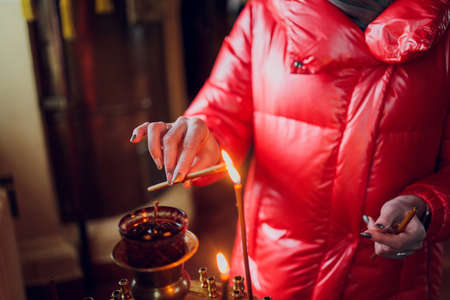 Womans hand in a red jacket puts a church candle.の写真素材