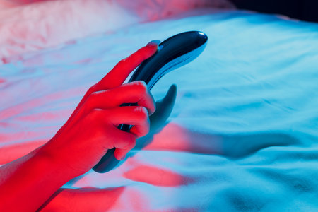 Woman in bedroom holding vibrator in hand.