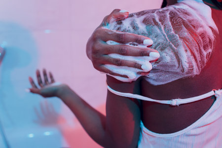 Pretty smiling black girl applying cream on her shoulder, body care concept.
