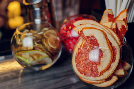 Glass jar with dried red grapefruit citrus slices on table. Grey background with copy space.