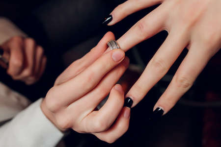 The groom puts a ring on the brides hand. Newlyweds exchange rings, groom puts the ring on the brides hand in marriage registry office . The brides is wearing a ring on the brides hand . Engagement.の写真素材