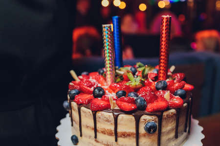 Birthday cake with candles. Candles on cake. Cake for holiday. Beautiful white cake with strawberries on dark background. Vertical photo.の写真素材