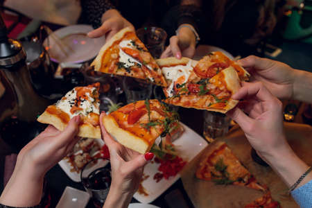 Friends taking slices of tasty pizza from plate, close up view.の写真素材