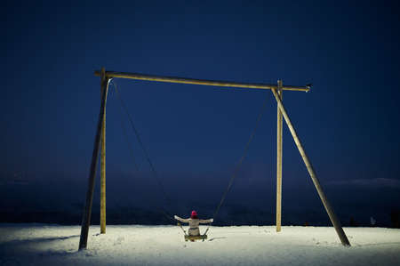 Playground swing with thick snow on ground and views of mountain and cloudy sky.の写真素材