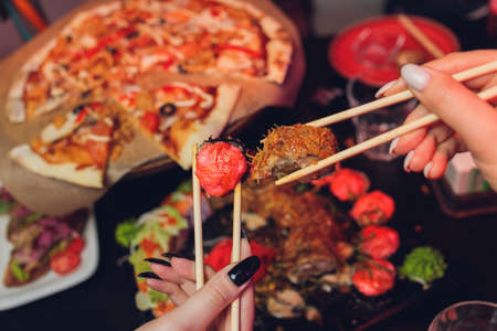 Young couple with chopsticks takes sushi from a plate in a japanese restaurant. Men and women starts eats japanese food. Focus on the seafood plate, close-up.の写真素材