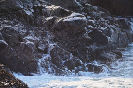 Small sea waves break against the stones of the shore. A bright sunny day and white foam of the...