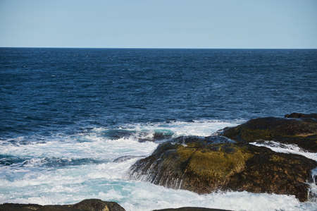 Small sea waves break against the stones of the shore. A bright sunny day and white foam of the...
