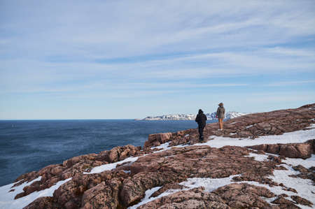 Portrait from back of warmly dressed woman in defocus standing in front of sea looking far away...