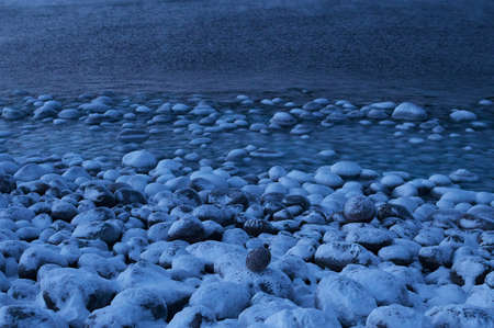 Small sea waves break against the stones of the shore. A bright sunny day and white foam of the waves. Melting glaciers as an environmental impact of air pollution.の写真素材