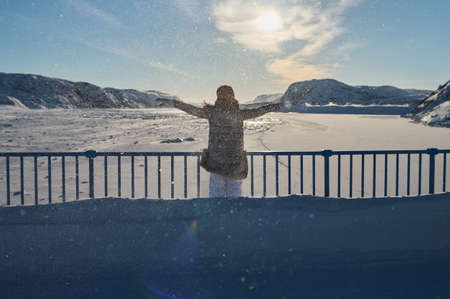 Portrait from back of warmly dressed woman in de-focus standing in front of sea looking far away...