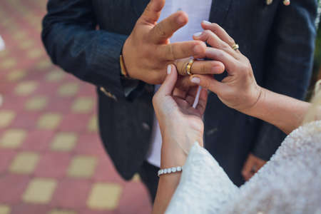 Bride putting a wedding ring on grooms finger.