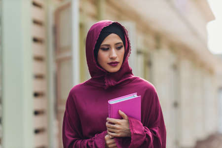 Confident Arab businessman smiling and walks of Dubai. Arab Business vumen hijab is in the streets against the skyscrapers of Dubai. The woman is dressed in a black abaya.の写真素材