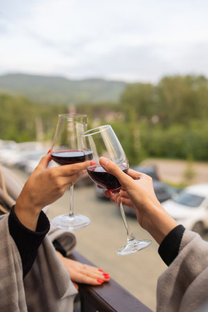 Two people clinking with glasses of red wine, celebrating success or speaking toast in wine restaurant, against racks with wine bottles, close up.の写真素材