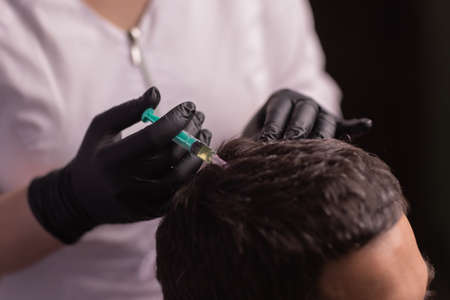 Mesotherapy for hair. Attractive man receiving injections in his head. Man having mesotherapy session at beauty salon, therapist in protective glove with syringe,の写真素材