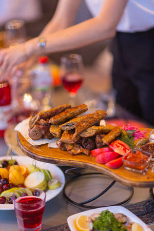 Wooden board with hot roasted pork ribs and sausages, decorated with fresh marjoram.