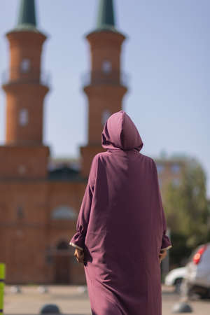 Islamic beautiful woman in a Muslim dress standing on a summer park street background forest autumn...